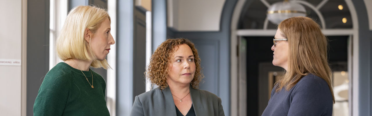 Three professional women facing each other, in conversation