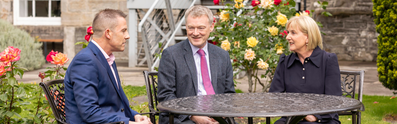 Professional men and a woman sitting at a garden table, in conversation
