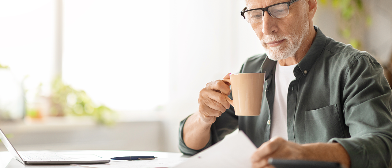 An older man reviewing a document with a laptop nearby